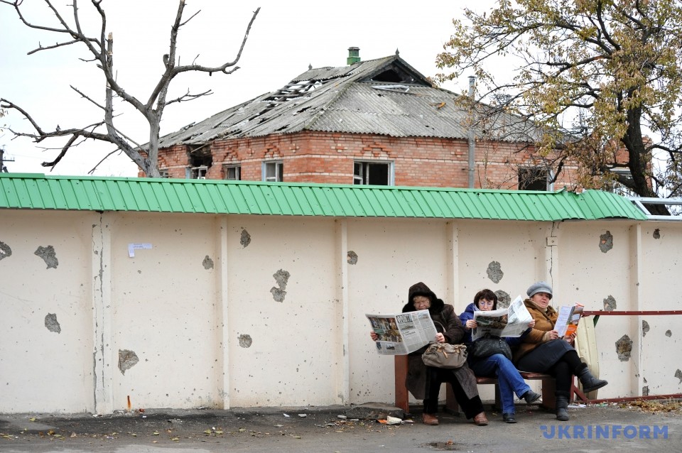 Женщины читают прессу на фоне разрушенного в результате обстрелов дома в пгт Станица Луганская, 27 октября 2015 года. Фото: Станислав Михайлов/Укринформ