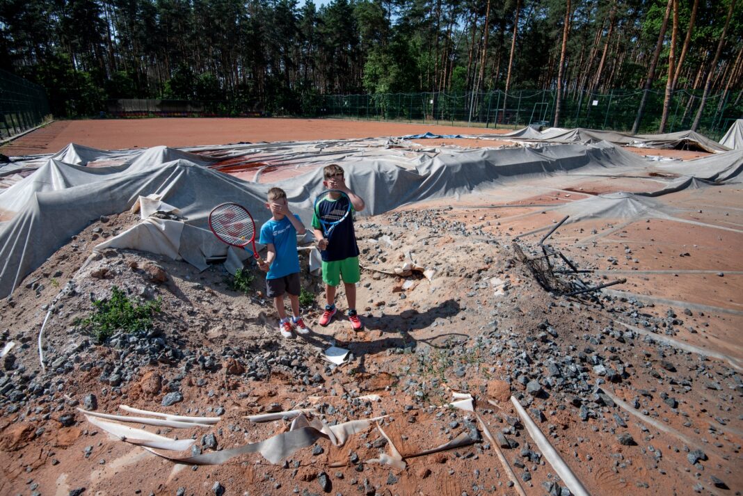 Два тенісисти стоять у вирві від вибуху посеред тенісного корту в Ірпені