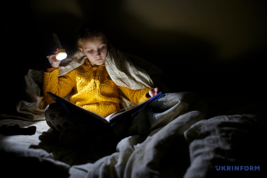 Восьмирічна Алевтина, батьки якої в 2014 році, рятуючись від війни, переїхали з Луганська в Ужгород, з ліхтариком читає книжку під час відключення електроенергії. Фото: Сергій Гудак