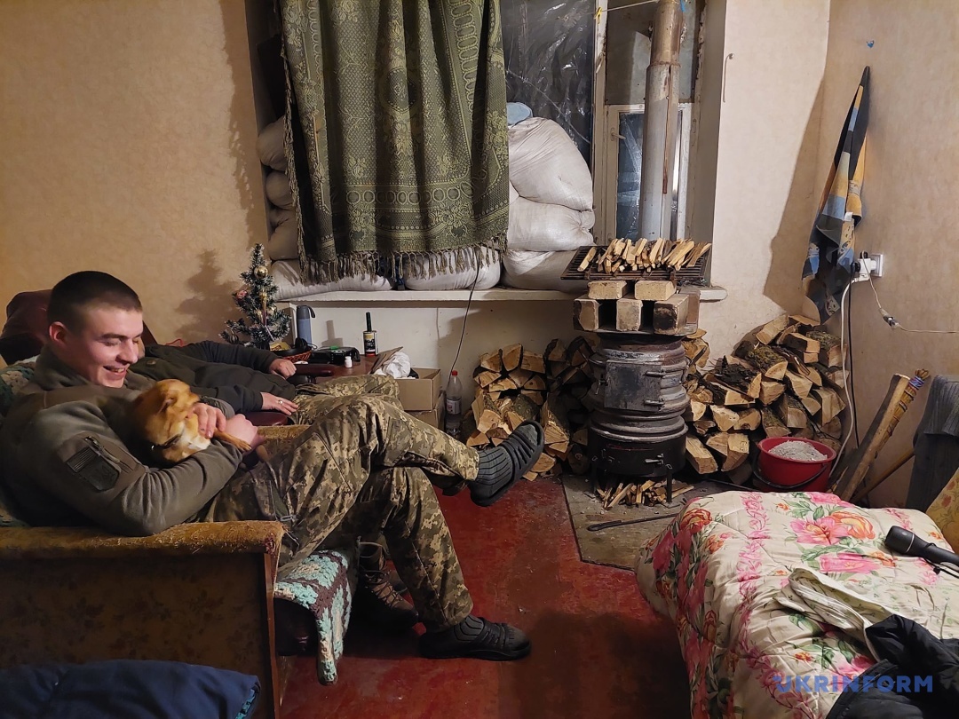 Боєць з позивним “Зуб” гріється з собакою Крим у вітальні біля буржуйки