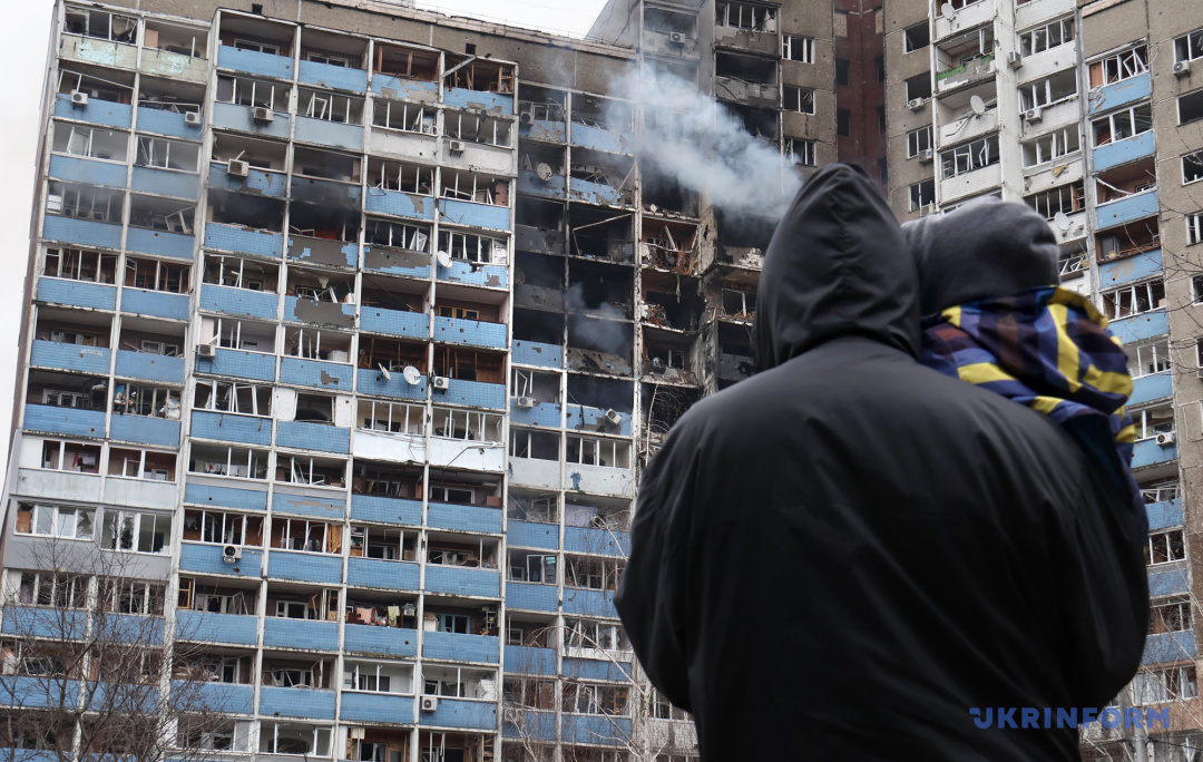 Mężczyzna z dzieckiem na rękach patrzy na wielopiętrowy budynek mieszkalny w stołecznej dzielnicy Holosijewskiej, który został uszkodzony w wyniku rosyjskiego ataku rakietowego, Kijów, 7 lutego 2024 r.