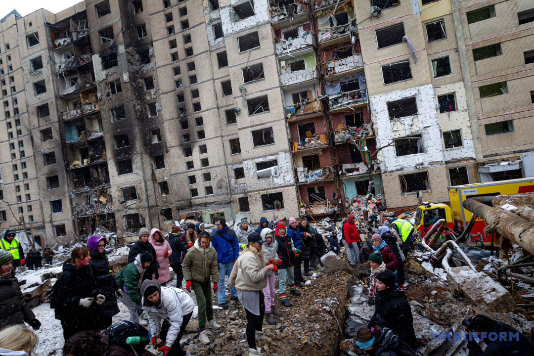 Miejscowi mieszkańcy i ochotnicy w pobliżu zniszczonego budynku mieszkalnego podczas likwidacji skutków rosyjskiego ostrzału w stołecznej dzielnicy Sołomienskiej, Kijów 3 stycznia 2024 r.