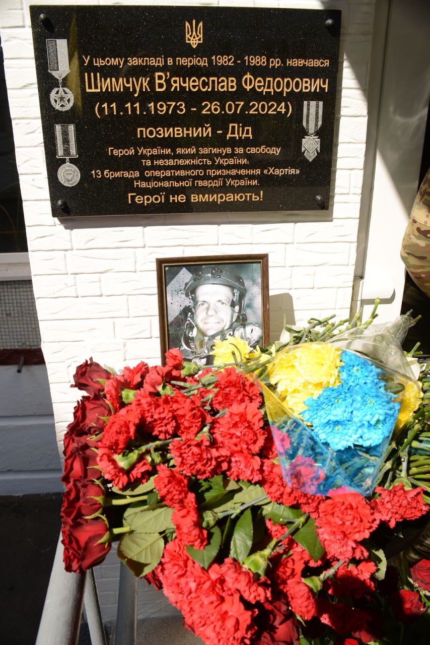 На стіні навчального закладу встановлено меморіальну дошку В’ячеславу Шимчуку з позивним «Дід», який навчався тут у 1982–1988 роках. Під дошкою розміщено його портрет і покладено численні квіти, зокрема букети в кольорах українського прапора. Фото з відкриття меморіальної дошки В’ячеславу Шимчуку, 30 квітня 2025 року / джерело: Харківська міська рада